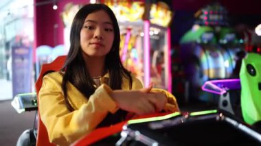 Atari salonunda oturan kendinden emin genç kız, elleri direksiyonda, canlı neon ışıklarla çevrili..