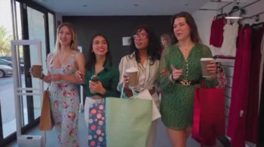 Dört kadın bir butikte alışveriş yaptıktan sonra alışveriş poşetleri ve kahveyle gülümseyip sohbet ediyorlar. Birlikte vakit geçiriyorlar. Bir Giyim Mağazasında Torba ve Kahveyle Alışveriş yapan Bir Kadın Grubu