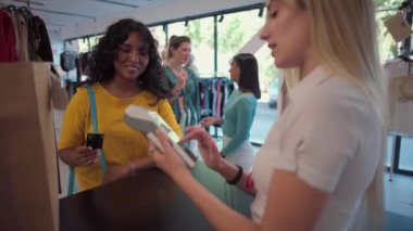 20 'li yaşlarda genç bir kadın giyim mağazasında kasiyer asistanlık yaparken isimsiz bir kart ödemesi yapıyor..