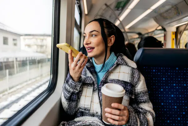 stock image A cheerful woman holds a coffee cup and talks on her smartphone during a train journey, enjoying the view outside.