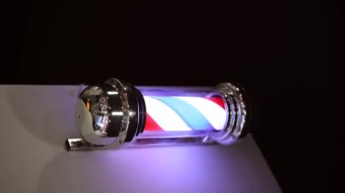 Geleneksel bir berber dükkanını sembolize eden kırmızı, beyaz ve mavi çizgili klasik bir berber direğine yakın plan..