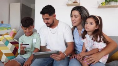 Gülümseyen Latin Amerikalı aile online alışveriş için tablet kullanıyor. Oğlu kredi kartı tutuyor ve ailesi izliyor..