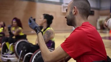 Erkek koç bir grup kadın tekerlekli sandalye basketbol oyuncusunu spor salonunda antrenman yaparken izliyor.