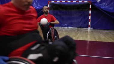 Tekerlekli sandalyedeki sporcu, bir spor salonunda rugby antrenmanı sırasında topu tutuyor.