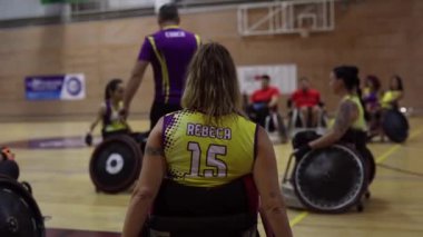 Tekerlekli sandalyede oturan, sarı ve mor üniformalı bayan bir basketbolcu maç boyunca sahada bekliyor.