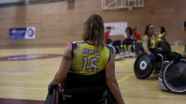 Engelli bir bayan sporcu, tekerlekli sandalye basketbol maçı sırasında takım arkadaşlarıyla birlikte sahada bekliyor.
