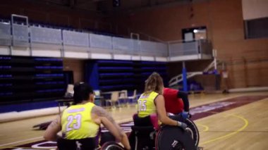 Tekerlekli sandalyedeki basketbol oyuncuları maç sırasında ara veriyorlar, gülümsüyorlar ve konuşuyorlar.