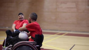 Tekerlekli sandalyede rugby oynayan iki sporcu pas veriyor.