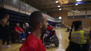 Tekerlekli sandalyedeki basketbolcu arka planda takım arkadaşlarıyla maçı izliyor.