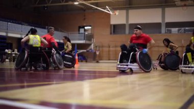 Tekerlekli sandalyedeki rugby oyuncuları spor salonunda birlikte antrenman yapıyorlar.