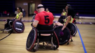 Tekerlekli sandalyedeki sporcular maçın kapalı basketbol sahasında başlamasını bekliyorlar.