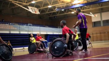 Tekerlekli sandalyede rugby oynayan sporcular mola sırasında antrenörlerini dinliyorlar.