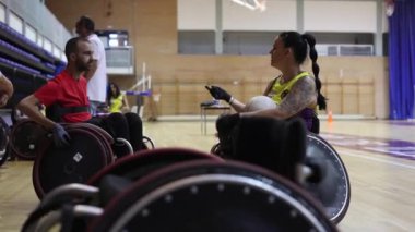 İki tekerlekli sandalyeli basketbolcu antrenman aralarında sohbet ediyorlar.