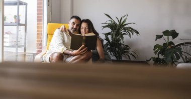Oturma odasındaki çift rahatlatıcı bir öğleden sonra kitap okuyup birbirlerine olan sevgilerini ve birlikte kaliteli zaman geçirmenin önemini gösteriyorlar.