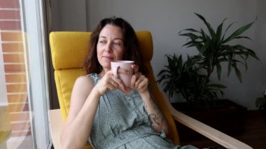 Kadın bir an için pencerenin yanındaki sandalyeye oturmuş elinde çay fincanı tutarak gözlerini kapatıyor.