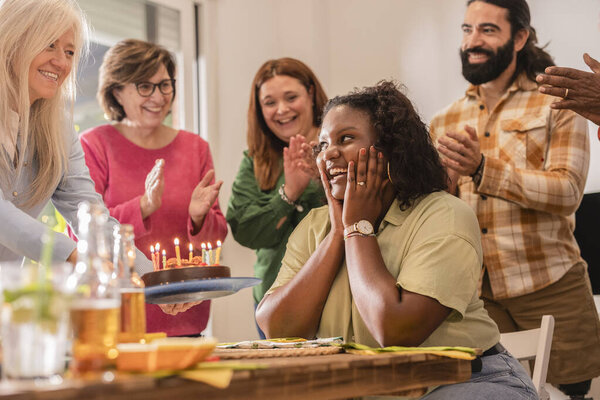 Diverse group of friends surprises their friend with a birthday cake, sharing joy and laughter in a warm and inviting setting