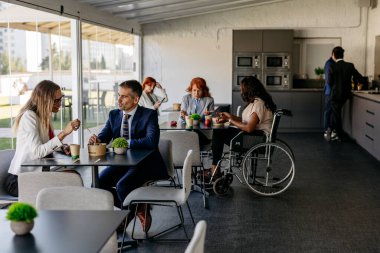 Çeşitli iş adamları, modern bir ofis kafeteryasında yemek ve sohbetin keyfini çıkararak, olumlu ve kapsayıcı bir çalışma ortamı yaratıyorlar.