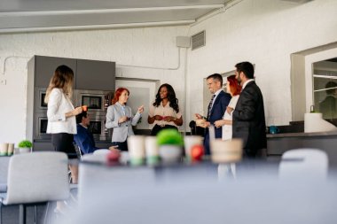 Çeşitli iş adamları ofis mutfağında dinlendirici bir kahve molası verip sohbet ediyorlar ve dostluk kuruyorlar.