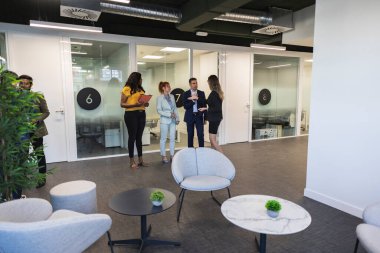 Çeşitli iş adamları modern ofis koridorlarında profesyonel ve işbirlikçi bir atmosfer yaratarak sohbet ediyorlar.