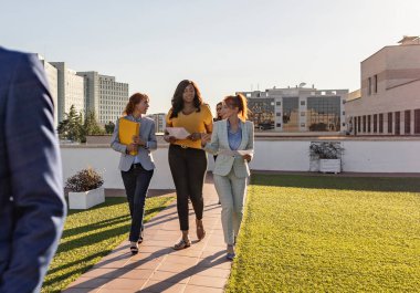 Bir grup iş kadını terasta yürürken temiz hava ve güneşin tadını çıkarıyorlar.