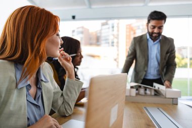 Mimarlardan oluşan çok ırklı bir ekip, bir binanın ölçekli modeline odaklanan ve işleri için dizüstü bilgisayar kullanan bir projeyi tartışıyorlar.