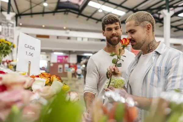 Mutlu eşcinsel çift çiçek pazarında güzel bir portakal gülü kokluyor. Çiçek seçerken romantik bir anın tadını çıkarıyorlar.