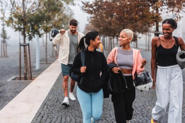Dört sportif arkadaş antrenmanlarından sonra şehirde birlikte yürüyüp sohbet ediyorlar, spor malzemelerini taşıyorlar ve şehir manzarasının tadını çıkarıyorlar.