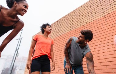 Üç mutlu sporcu, şehirde antrenman yaparken ara verip sohbet ediyorlar. Arkadaşlık ve şehir sporlarının tadını çıkarıyorlar.