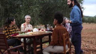 Çok ırklı çiftçiler zeytin bahçesinde birlikte yemek yiyorlar, zeytin hasadı yaptıktan sonra, emeklerinin meyvelerini taze yiyecek ve içeceklerle yiyorlar.
