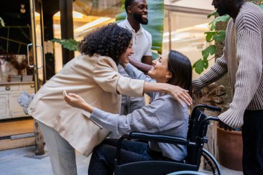 Çeşitli iş arkadaşları, iş yerinde destek ve kapsayıcılık gösteren tekerlekli sandalyedeki bir meslektaşlarını sıcak bir şekilde karşılıyor.