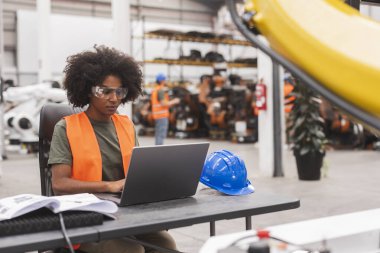 Genç Afro-Amerikan kadın mühendis güvenlik gözlüğü ve yelek programlama dizüstü bilgisayarı takıyor.