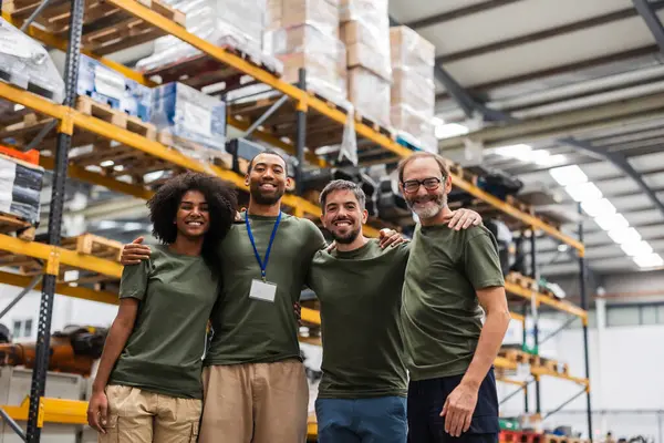 Robot mühendislerinden oluşan çok ırklı bir ekip birbirlerine sarılıyor, gülümsüyor ve büyük, modern, yüksek teknoloji fabrikasında birlikte çalışıyorlar.