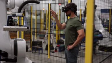 VR gözlük takan mühendis, modern endüstriyel bir fabrikada otomasyon ve kesinlik için ileri teknoloji entegre eden bir robotik kolu kontrol etmek ve programlamak için sanal gerçeklik kulaklığı kullanıyor.