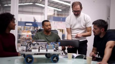 Çok nesilli ve çok ırklı mühendisler modern fabrika ortamında bir robotik projesinde birlikte çalışıyorlar. Tablet ve dokümanları kullanarak ilerlemelerini tartışıyor ve analiz ediyorlar.