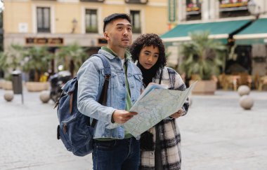 Sevgililer Günü tatilinin tadını çıkaran çok ırklı iki turist, bir harita tutarken günlük giysiler giyiyorlar ve yeni bir şehrin canlı sokaklarını keşfediyorlar.