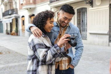 Dışarıda güneşli bir günün tadını çıkaran genç bir çift, sevgililer gününde kucaklaşırken ve gülerken dijital kamerayla neşeli anları yakalıyorlar.