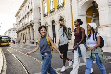 Sırt çantalı dört mutlu turist Lizbon 'da bir tramvayın yanında yürürken ve karşıdan karşıya geçerken bir adam arkadaşlarına bir şey gösteriyor.
