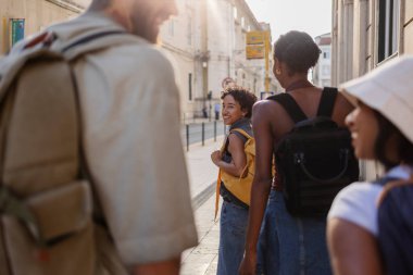 Lizbon, Portekiz 'de güneşli bir sokakta yürüyen bir grup genç turist, birlikte şehrin canlı kültürünü ve manzarasını keşfederken kahkahalarını ve anılarını paylaşıyorlar.