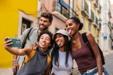 Sırt çantalı dört neşeli genç turist dillerini uzatarak selfie çekiyorlar. Lisbon 'daki tatillerinde birlikte eğleniyorlar. Portekiz. Şehrin canlı atmosferinin tadını çıkarıyorum.