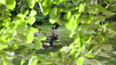 Bir grup neşeli çoklu etnik arkadaş huzurlu bir bahçede hamakta gevşeyip sohbet ediyorlar. Güneşli bir günde, yemyeşil bir havanın tadını çıkarıyorlar.