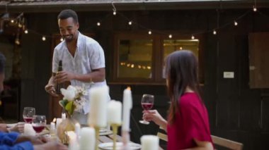 Mutlu çeşitli arkadaşlar, dışarıda güzel dekore edilmiş bir masada oturmuş arkadaşlıklarını kutlarken bir kadeh kırmızı şarapla kadeh kaldırıyorlar.