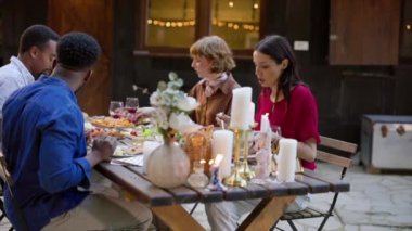 Dört arkadaş kırsal bir ahşap masanın etrafında toplanıp mum ışığının sıcacık parıltısı altında lezzetli bir şarküteri tahtası, şarap ve sohbetin tadını çıkarıyorlar.