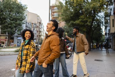 Muhtemelen gezginler ya da öğrenciler olmak üzere dört neşeli çoklu etnik yetişkin arkadaş, kaldırımda birlikte yürüyor ve gülüyorlar, yeni bir şehir ortamını keşfetmek için zamanlarının tadını çıkarıyorlar.