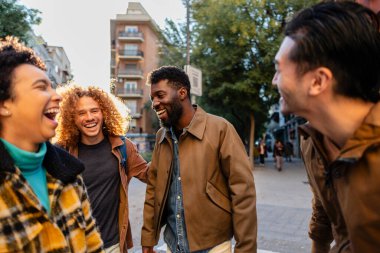 Dört neşeli çoklu etnik arkadaş, öğrenciler ya da gezginler, güneşli bir günde birlikte yürüyüp gülüyorlar.