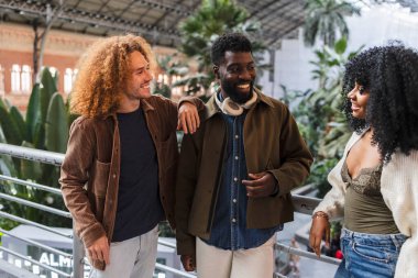 Üç genç çok ırklı arkadaş, iki erkek ve bir kadın, Madrid, İspanya 'daki tren istasyonunda yürüyorlar ve konuşuyorlar, trene binmeden önce birlikte vakit geçiriyorlar.