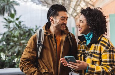 İki genç öğrenci tatillerinin tadını çıkarıyorlar. Bir akıllı telefona danışarak gülümsüyorlar. Seyahat edecekleri yeri keşfederken eğlenceli bir anı paylaşıyorlar.