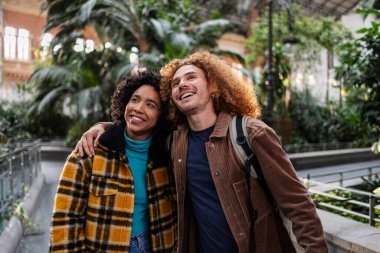 Genç çoklu etnik çiftler kucaklaşıp yukarı bakıyorlar, Madrid, İspanya 'daki tropikal bahçenin tadını çıkarıyorlar.