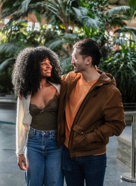 Atocha istasyonunda gülümseyen ve birlikte yürüyen çok ırklı genç bir çift, Madrid, İspanya, tropikal bitki ve bitkilerle dolu ünlü bir turistik mekan.