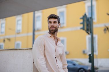 Dövmeleri ve kulaklıkları olan şık genç adam Lizbon 'un kentsel atmosferini seviyor. Rahat bir duruş ve düşünceli bir ifadeyle duvara yaslanıyor.