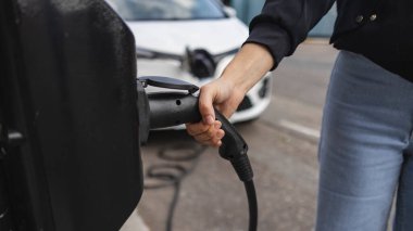 Elektrikli bir aracın kablosunu tutan bir kadının elini kapatın, Londra 'daki bir şarj istasyonuna bağlayın, sürdürülebilir ulaşım ve çevre dostu uygulamalar sergileyin.